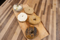 Wooden board with four bagel halves, some topped with seeds, beside a bowl of cream cheese