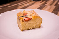 Square slice of Bublanina (Czech Bubble Cake) with strawberry slices and powdered sugar on a white plate.