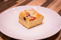 Square slice of Bublanina (Czech Bubble Cake) with strawberries and dark berries, dusted with powdered sugar.