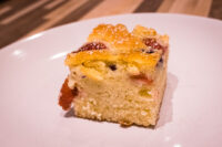 Square slice of Bublanina (Czech Bubble Cake) with baked fruit pieces and a glazed top, on a white plate.