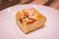 Slice of Bublanina (Czech Bubble Cake) with strawberries and dark berries, dusted with powdered sugar, on a plate.
