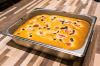 Baked Bublanina (Czech Bubble Cake) with strawberries and blueberries in a metal pan on a wooden counter.