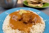 Butter Chicken chunks in orange-brown sauce over rice on a blue plate, garnished with julienned strips.