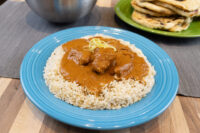 Butter Chicken pieces in brown curry sauce over rice, topped with citrus zest, on a blue plate.