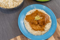 Butter Chicken sauce with meat chunks over rice on a blue plate, garnished with lemon zest.