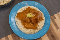 Butter Chicken chunks in orange-red sauce over rice on a blue plate, garnished with yellow zest.
