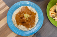 Butter Chicken sauce with chicken pieces over rice on a blue plate, garnished with lemon zest.