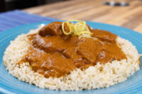 Butter Chicken in tomato sauce over white rice, garnished with yellow shreds, on a blue plate.