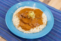 Butter Chicken pieces in tomato sauce over rice, garnished with julienned strands, on a blue plate