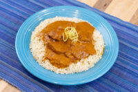 Butter Chicken pieces in a brown tomato-based sauce served over white rice on a blue plate.