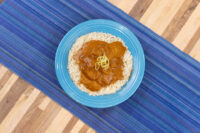 Butter Chicken curry sauce with meat ladled over rice on a blue plate, topped with thin garnish strands