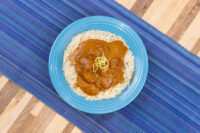 Butter Chicken in orange-brown sauce over rice on a blue plate, garnished with fine shredded zest.