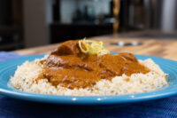 Blue plate of Butter Chicken in tomato gravy over herbed rice, topped with citrus zest.