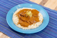 Butter Chicken pieces in orange-brown sauce over rice on a blue plate, garnished with shredded strands