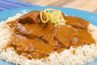 Butter Chicken pieces in thick tomato sauce over rice, topped with shredded ginger, on a blue plate.