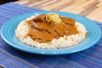 Butter Chicken chunks in thick brown sauce over rice, topped with yellow garnish strands, on a turquoise plate