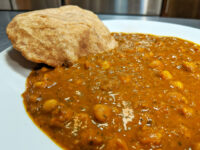 Chana Masala chickpea curry in thick gravy on a white plate, served with puffed fried bread.