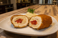 Sliced Chicken Cordon Bleu with red pimento filling, served with piped mashed potatoes and parsley on a white plate.
