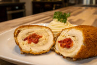 Sliced Chicken Cordon Bleu halves with red pimento filling, served with piped mashed potato and parsley.