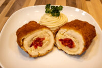 Sliced Chicken Cordon Bleu showing cheese and pimento filling, served with piped mashed potato and parsley.