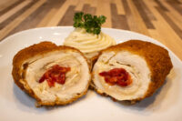 Sliced Chicken Cordon Bleu showing melted cheese and pimento pepper filling, plated with piped mashed potato.