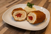 Sliced Chicken Cordon Bleu on a white plate showing cheese and pimento filling, with piped mashed potato and parsley.