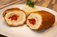 Sliced Chicken Cordon Bleu showing cheese and pimento filling, served with piped mashed potato on a white plate