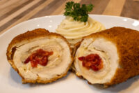 Sliced Chicken Cordon Bleu with red pimento filling, plated with piped mashed potatoes and parsley.