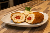 Sliced Chicken Cordon Bleu roll with melted cheese and red pepper filling, served with mashed potatoes and parsley.