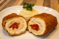 Sliced Chicken Cordon Bleu showing red pimento filling, plated with a mashed potato swirl and parsley.