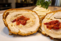 Sliced Chicken Cordon Bleu showing melted cheese and pimento pepper filling, with mashed potato and parsley behind.