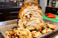 Golden roasted Chicken Gyros loaf sliced open on a metal tray, with shredded meat piled beneath.