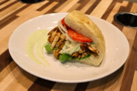 Chicken Gyros sandwich on a crusty roll with grilled chicken, tomato, onion, greens, and green sauce.