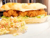 Crispy chicken tenders sandwich with melted cheese and lettuce on a toasted bun, served with coleslaw.