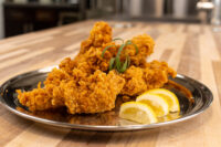 Crispy Chicken Tenders piled on a metal plate with lemon wedges and a green herb garnish.