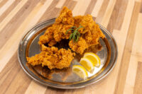 Crispy fried Chicken Tenders piled on a metal plate with lemon wedges and a green herb garnish