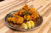 Golden crispy Chicken Tenders piled on a metal plate with lemon wedges and a herb garnish.