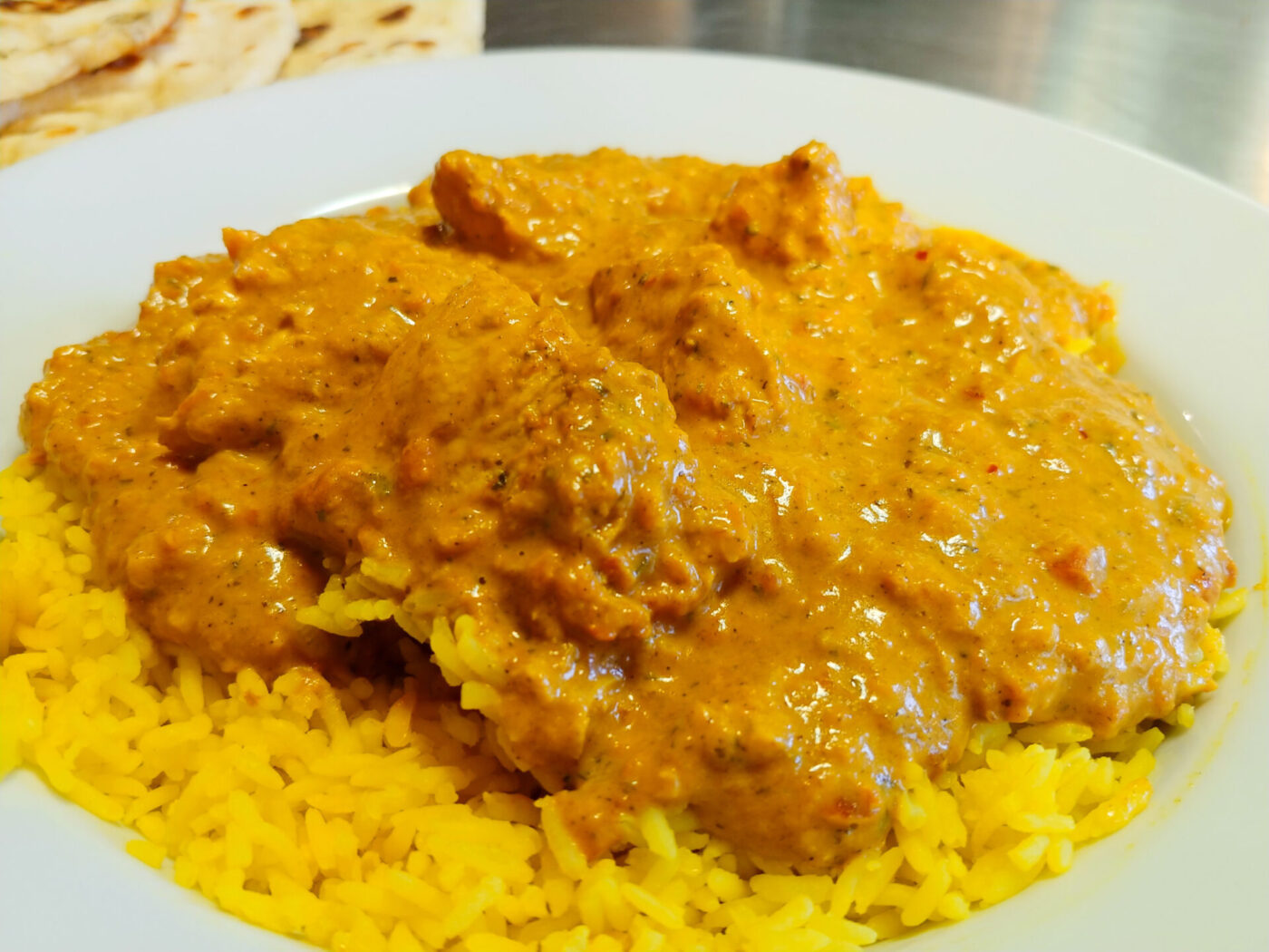 Chicken Tikka Masala in creamy orange sauce spooned over yellow rice on a white plate.