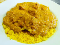 Chicken Tikka Masala in creamy orange sauce served over turmeric yellow rice on a white plate.
