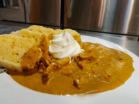 Creamy Paprika Chicken Kuře na Paprice with sour cream on a plate beside sliced dumpling bread.