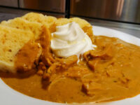 Plate of Creamy Paprika Chicken Kuře na Paprice with shredded chicken in paprika sauce, whipped cream, and bread dumplings.