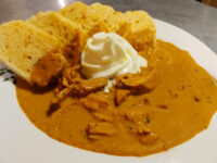 Bowl of Creamy Paprika Chicken Kuře na Paprice with shredded chicken, sour cream dollop, and toasted bread slices.