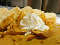 Bowl of Creamy Paprika Chicken Kuře na Paprice with a whipped cream dollop, ringed by bread slices