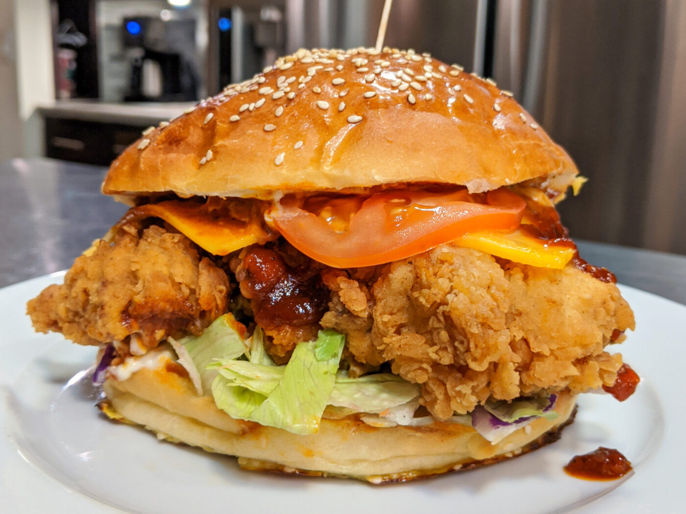 Crispy Chicken Sandwich with BBQ Sauce on a sesame bun with lettuce, tomato, cheese, and red sauce.