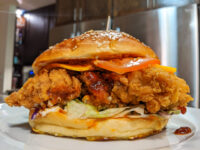 Crispy Chicken Sandwich with BBQ Sauce cut open, showing fried chicken, cheese, sauce, and slaw on a sesame bun.