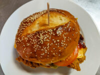 Crispy Chicken Sandwich with BBQ Sauce on a sesame bun with cheese and tomato, held with a skewer.