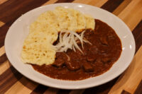 Bowl of Czech Beef Goulash with tender beef chunks, raw onion strips, and torn bread on a white plate.