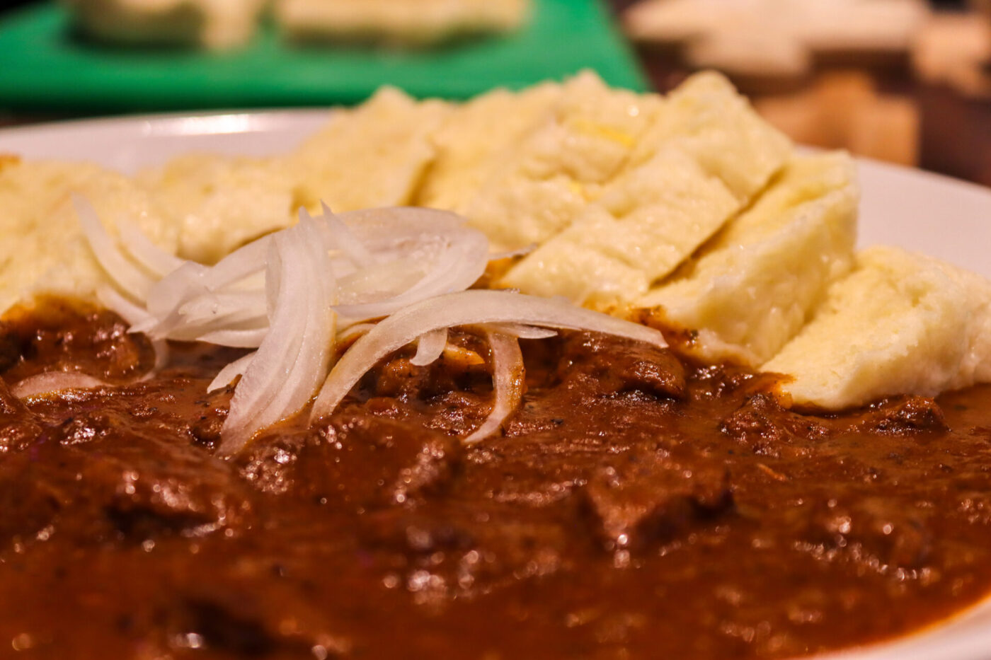 Close-up of Czech Beef Goulash topped with raw onion slices, served with squares of bread on a white plate