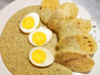 Czech Dill Sauce Koprová Omáčka poured over dumpling slices with three halved eggs on a leaf-patterned plate