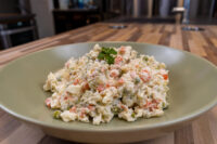Bowl of Czech Potato Salad with diced potato, carrot, and peas in creamy dressing, topped with parsley.